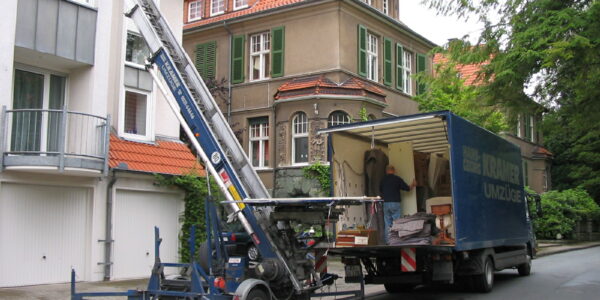 Ein Umzugswagen des Unternehmen KRAMER Umzüge und ein Lastenaufzug stehen vor einem Haus.
